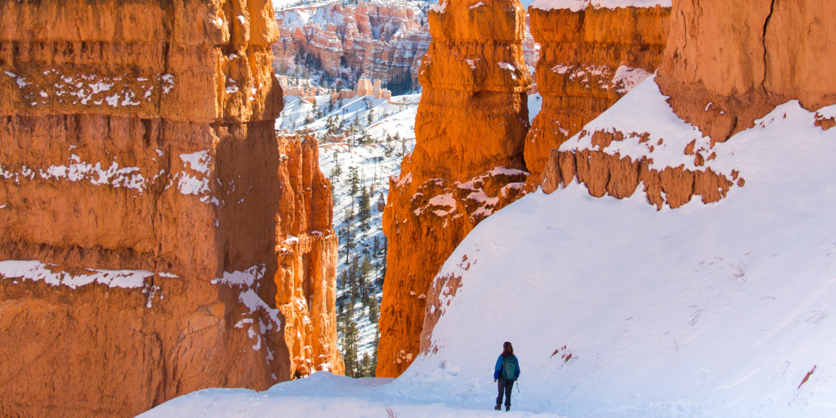 A woman hikes in the snow between two hoodoos