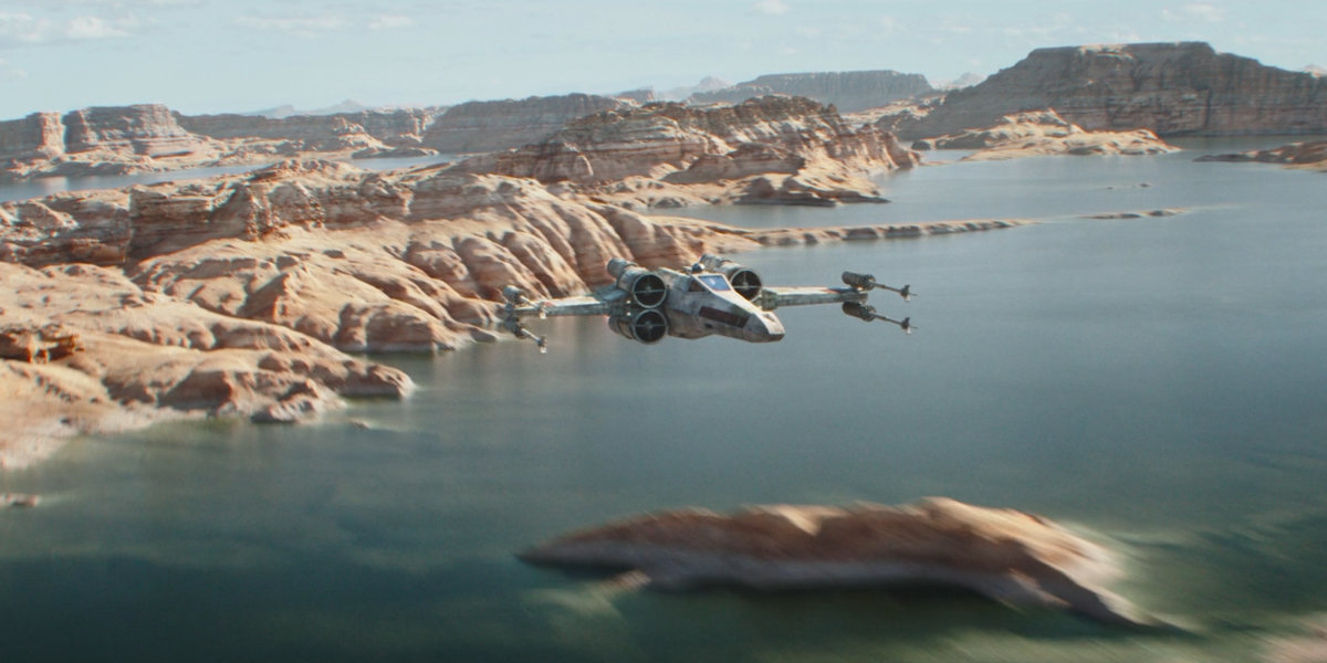 An x-wing fighter flies over a lake